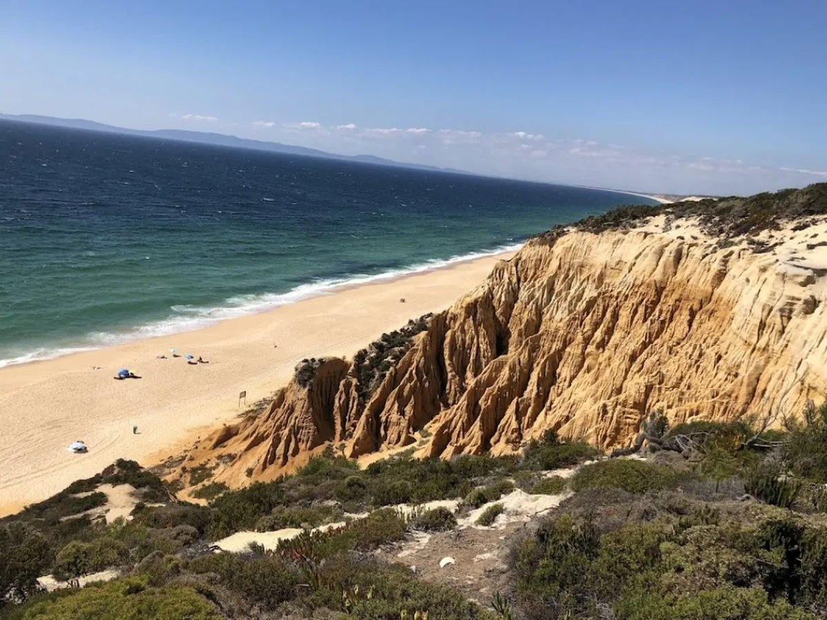 The wild Melides coast — ochre dune cliffs above an empty Atlantic beach